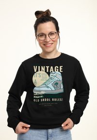 Felpa nera con una stampa grafica di una sneaker. Il testo in vari colori mette in risalto "VINTAGE" e "OLD SKOOL RULES!" sul davanti.