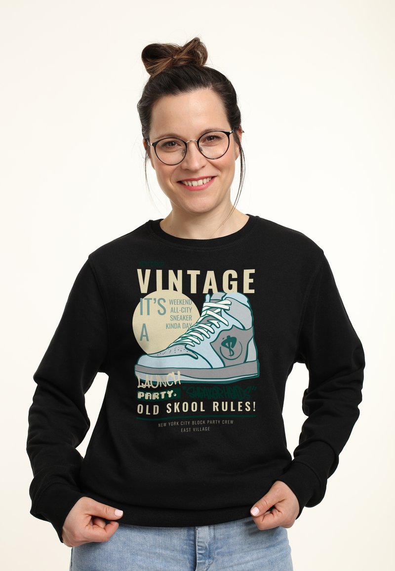 Felpa nera con una stampa grafica di una sneaker. Il testo in vari colori mette in risalto "VINTAGE" e "OLD SKOOL RULES!" sul davanti.