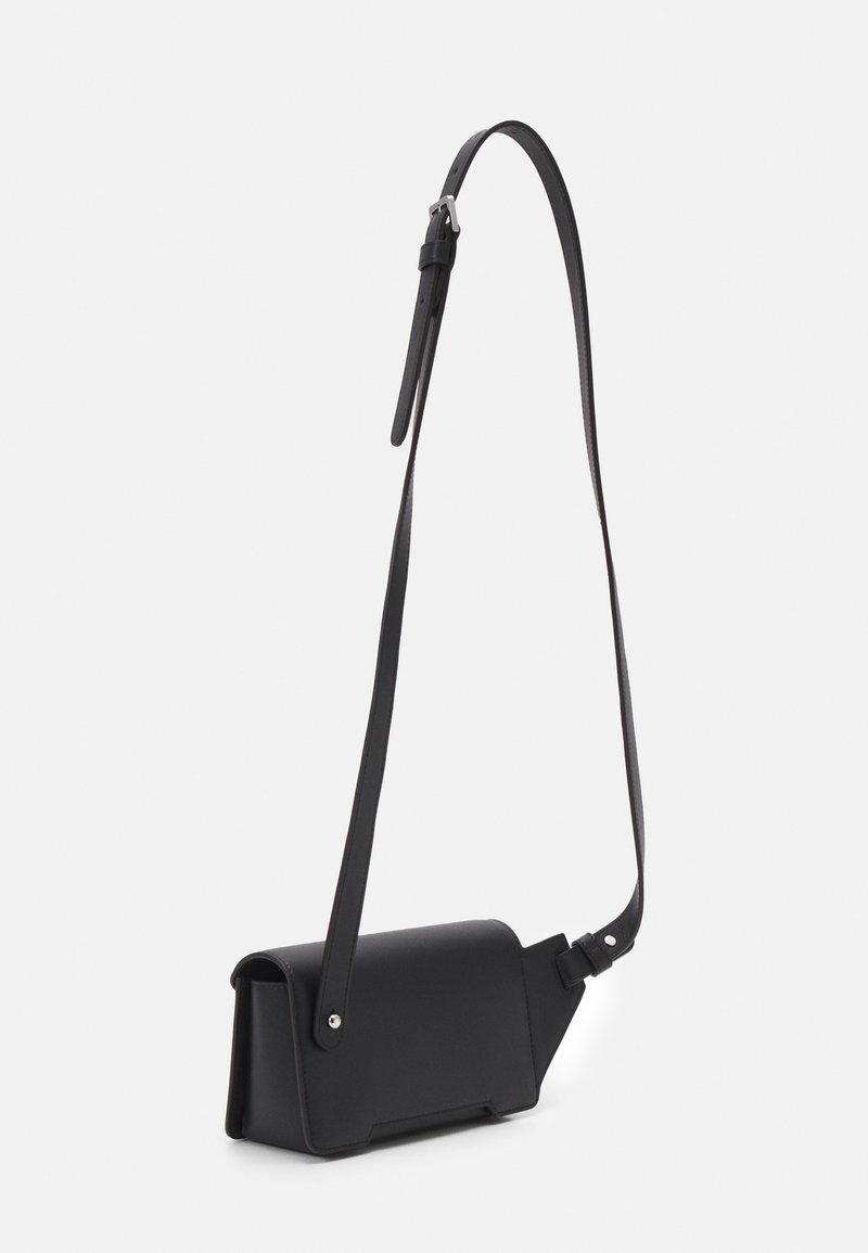 Sacoche en cuir noir à porter en travers avec une forme structurée, une sangle réglable et un design minimaliste. Elle dispose d'une fermeture à rabat et de quincaillerie en argent.