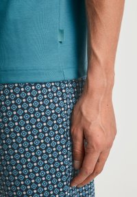 Teal T-shirt met korte mouwen met een subtiele textuur, gecombineerd met donkere shorts met een blauw bloemenpatroon en witte accenten.