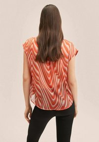 Top trasparente a maniche corte con un motivo ondulato rosso e bianco, orlo rotondo e tessuto leggero, abbinato a pantaloni neri aderenti.