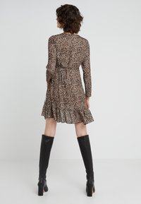 Robe à imprimé léopard avec des manches longues, un ourlet volanté et une taille à nouer. Associée à des bottes en cuir noir montantes à talon épais.
