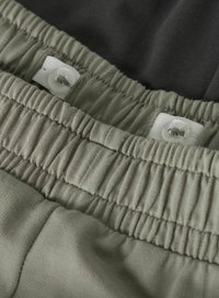 Ceinture élastique ajustable sur pantalon vert clair avec des boutons-pression sur un tissu blanc à l'intérieur de la taille.