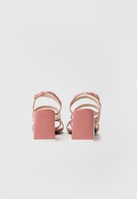 Pink heeled sandals with a square block heel and multiple strap design. Smooth texture with a polished finish and adjustable ankle strap.