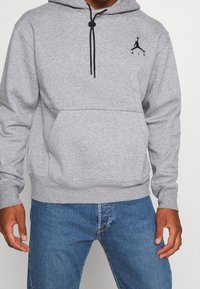 Felpa grigia con cappuccio, dotata di tasca kangaroo frontale, lacci neri e un piccolo logo nero sul petto. Tessuto morbido e vestibilità comoda.