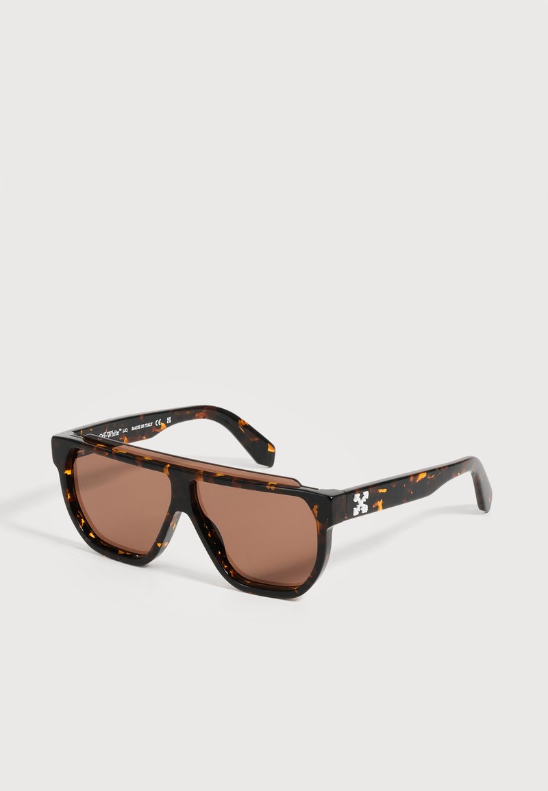 Lunettes de soleil à monture écaille foncée avec verres rectangulaires marron et logo blanc sur la branche, sur fond uni.