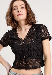 Top court en dentelle noire avec un motif floral, des manches courtes, un décolleté en V et des détails de boutons à l'avant. Matière douce et légère.