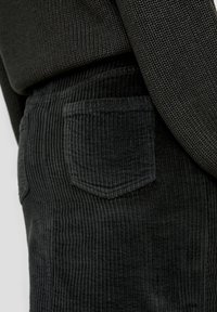 Schwarze Cordhosen mit feiner Ripptextur, ausgestattet mit einer einzelnen aufgesetzten Tasche auf der Rückseite. Der Stoff hat eine weiche, strapazierfähige Oberfläche.