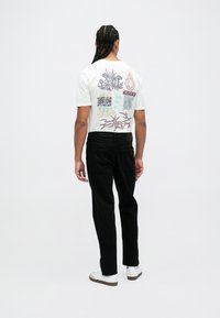 Camiseta de algodón blanca con gráficos coloridos en la parte trasera, combinada con pantalones negros y zapatillas blancas. Diseño minimalista, ajuste relajado.