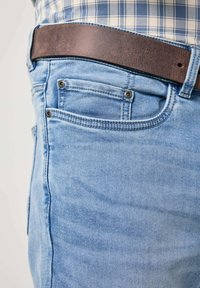 Jeans de mezclilla azul claro con un cinturón marrón. Presentan dos bolsillos frontales, costuras visibles y una textura suave.