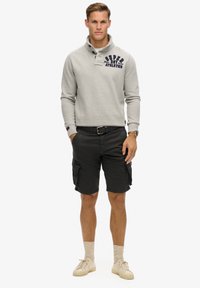 Szara bluza z kołnierzykiem, granatowy detal z logo, czarne szorty cargo z kieszeniami, beżowe sneakersy i jasne skarpety.