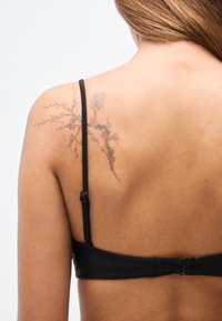 Soutien-gorge noir avec bretelles réglables et fermoir à crochets. Présente un effet peau texturée et un tatouage floral coloré sur l'épaule.