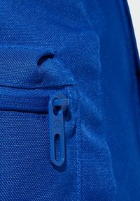Zaino in tessuto blu, caratterizzato da una superficie testurizzata, una tasca con zip dotata di una zip blu abbinata e cuciture rinforzate.