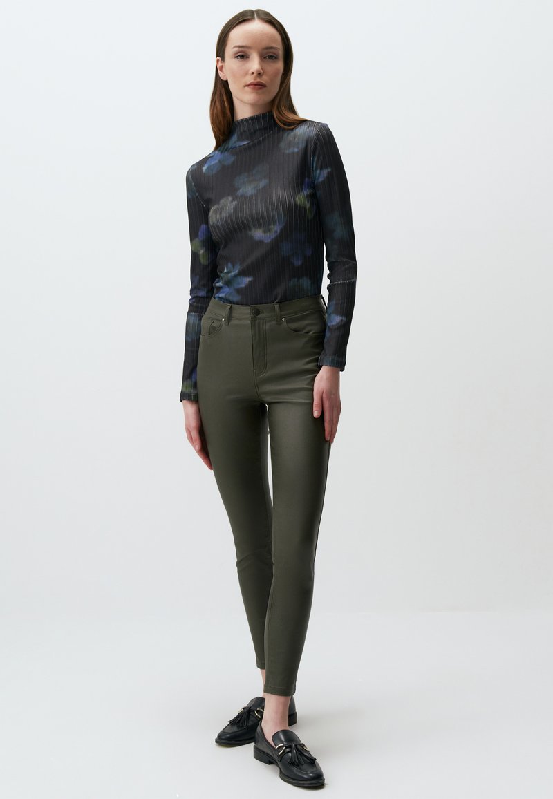 Geribbelde zwarte coltrui met bloemenpatroon; olijfgroene hoge taille skinny pants; zwarte schoenen met een decoratieve accenten.