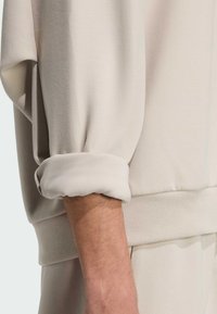 Felpa beige chiaro con una texture morbida, caratterizzata da polsini arrotolati, orlo a coste e vestibilità rilassata. Dettagli di design eleganti e minimalisti.