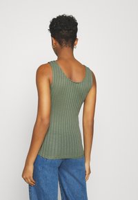Top verde a costine con scollatura ampia e aderente, con una finitura testurizzata. Abbinato a jeans a gamba larga blu chiaro.