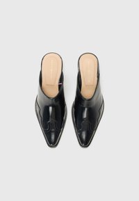 Mules de couro preto com bico apontado, costura decorativa, parte de trás aberta e palmilha em bege claro com o nome da marca em relevo.