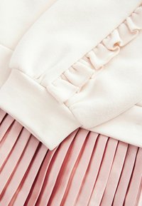 Helle, rosa Sweatshirt mit Rüschendetail an den Ärmeln, kombiniert mit einem plissierten Satintenü in einem dunkleren Rosaton, der weiche Texturen zeigt.