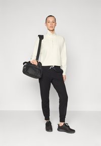 Lys beige quarter-zip genser, svarte tapered joggebukser og svarte treningssko, med en svart skulderveske med nettingdetaljer.