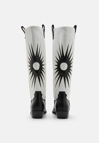 Knee-high boots with a glossy black base, white leather shaft, and black starburst pattern. Features rear pull tabs and square heels.