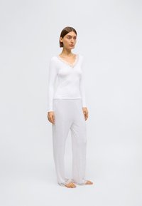 Biely top s dlhým rukávom a čipkovaným výstrihom v páre s voľnými nohavicami svetlošedej farby. Obe položky majú mäkkú tkaninu a jemnú čipkovú ozdobu.