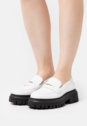 Mocassins blancs à bout rond, dotés d'une semelle noire épaisse, de détails cousus et d'un accent doré sur le dessus.