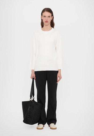 Biele rebrované tričko s dlhým rukávom, čierne nohavice s širokými nohavicami, tkaná čierna taška s štruktúrovaným povrchom a béžové tenisky.