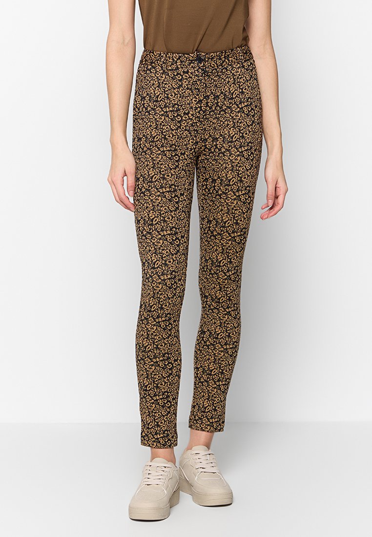 Schwarze Leggings mit floralem Muster in Beige und Braun. Hohe Taille, schmale Passform, aus dehnbarem Stoff. Getragen mit beigen Sneakers.