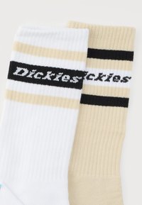 Ζευγάρι ριμπ πλεκτές κάλτσες μέχρι τον αστράγαλο, μία λευκή και μία μπεζ, η καθεμία με μαύρες και μπεζ ρίγες και το λογότυπο "Dickies" στις πάνω ταινίες.