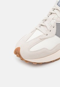 Light gray sneaker with suede and leather panels, textured sole, and tonal laces. Features a prominent design and rounded toe.