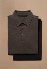 Polo cinza escuro feito de tecido texturizado, com colarinho e três botões, disposto em cima de uma camisa azul-marinho.