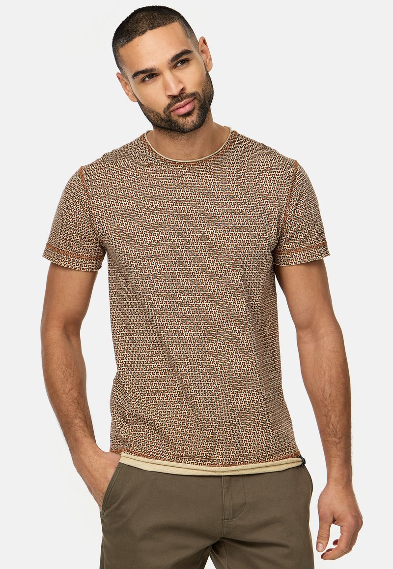 Kortærmet t-shirt i brune nuancer med et geometrisk mønster. Rund halsudskæring med lysfarvet kant og subtilt tekstureret stof.