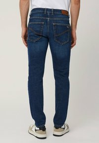 Jeans in denim blu scuro con vestibilità slim, caratterizzati da un patch in pelle sulla vita e due tasche posteriori con cuciture curve.