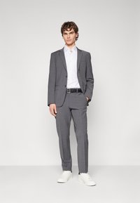 Giacca da completo a quadri grigi con pantaloni abbinati, camicia bianca con bottoni, cintura nera e sneakers bianche. Tessuto liscio con vestibilità su misura.