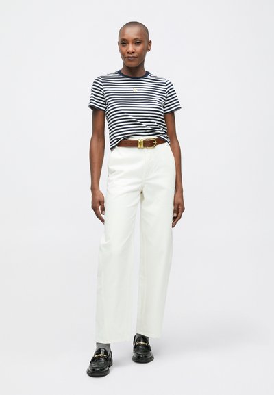 Prúžkované tričko v námorníckej a bielej farbe, vysoké biele nohavice, hnedý opasok so zlatou prackou a čierne mokasíny. Hladká textúra a uvoľnený strih.