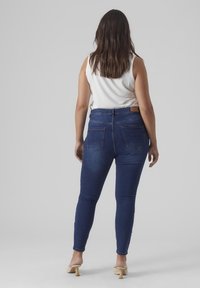 Dunkelblaue Skinny Jeans mit hoher Taille, ausgewaschenen Details und zwei Gesäßtaschen, kombiniert mit einem weißen ärmellosen Oberteil.