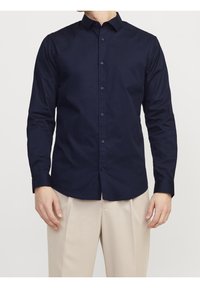 Camisa de manga larga azul marino hecha de algodón, con cuello clásico, cierre de botones en la parte delantera y textura suave. Se lleva con pantalones beige.