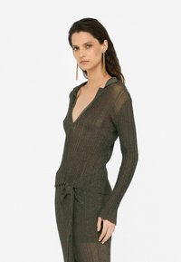 Bronzefarbenes, geripptes Stricktop mit tiefem V-Ausschnitt und Kragen, verfügt über lange Ärmel und einen gerafften Saum. Eine Bindung in der Taille rundet das Design ab.
