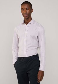 Camicetta bianca con motivo a quadri rossi e blu, colletto button-down e maniche lunghe, abbinata a pantaloni scuri blu navy.