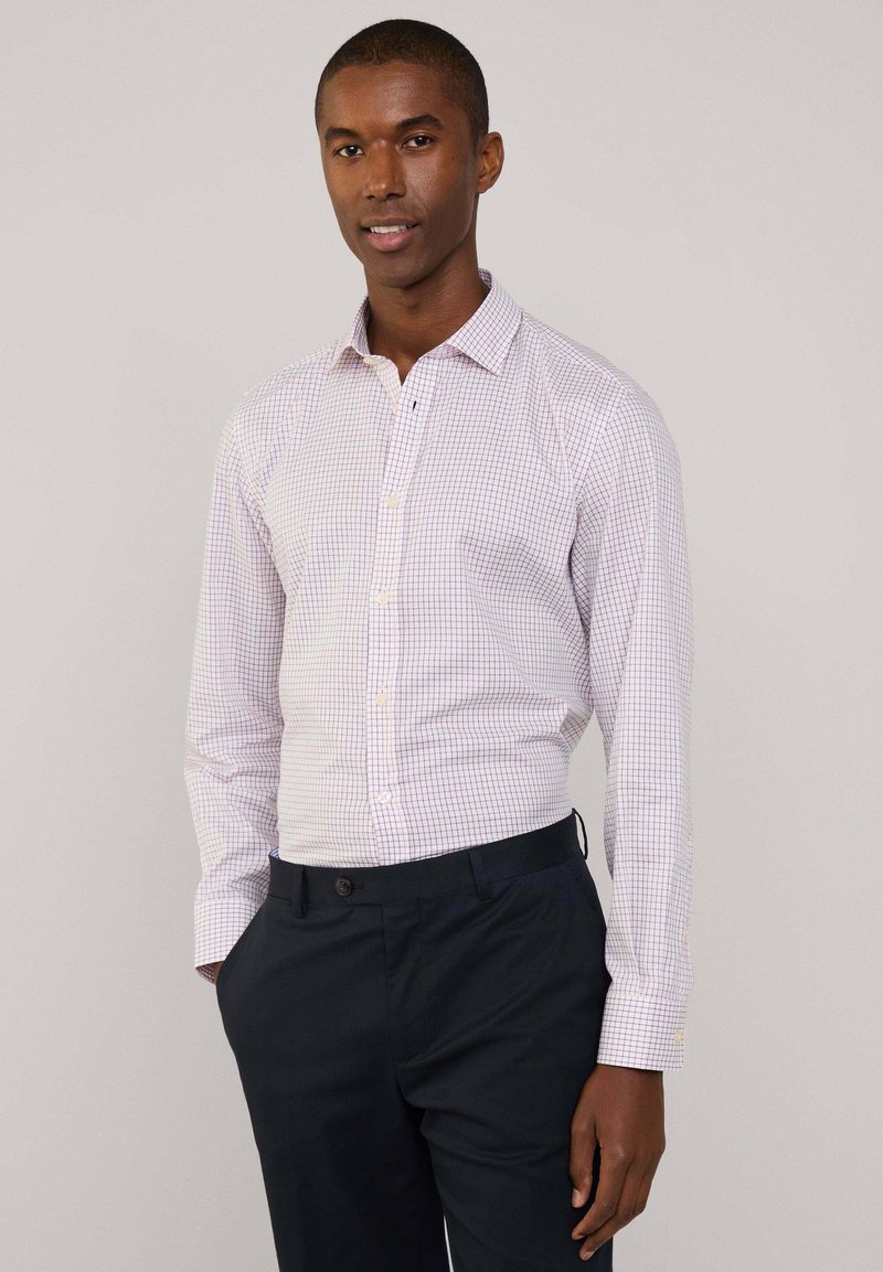 Camicetta bianca con motivo a quadri rossi e blu, colletto button-down e maniche lunghe, abbinata a pantaloni scuri blu navy.