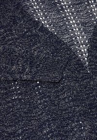 Cardigan lavorato a maglia navy con un motivo testurizzato caratterizzato da dettagli in openwork e una singola tasca sul petto. Tessuto morbido e leggero con una leggera lucentezza.