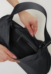 Borsa nera realizzata con materiali riciclati, dotata di chiusura con zipper, superficie liscia e una maniglia resistente, mostrata aperta con una mano all'interno.