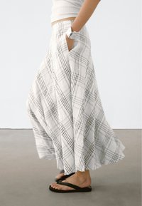 Jupe longue et fluide en tissu léger texturé. Blanche avec un motif à carreaux noirs, dotée de poches latérales et d'une coupe décontractée.