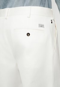 Fehér pamut nadrág sima felülettel, hátul gombos zsebbel és a derékrészen márkacímkével.