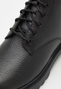 Stivale in pelle nera con finitura texturizzata, design con lacci e suola in gomma. Presenta occhielli rotondi e cuciture rinforzate lungo le cuciture.