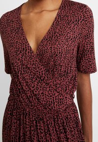 Gros plan sur une personne portant une robe à manches courtes et décolleté en V profond avec un motif léopard bordeaux et noir.