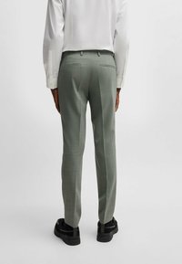 Pantalons ajustés gris clair avec une finition texturée, présentant une coupe droite et deux poches arrière, associés à des chaussures noires.
