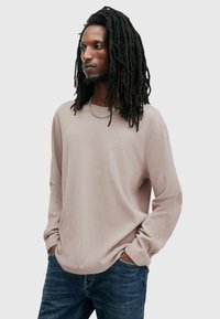 Šviesiai pilkas ilgomis rankovėmis marškinėliai su varžtų tekstūra, apvaliu kaklu ir siuvinėtu akcentu. Derinama su tamsiai mėlynomis džinsais.