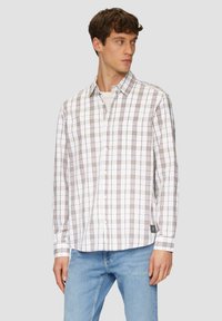 Chemise à carreaux blanche avec des lignes brunes, manches longues, poche poitrine unique et ourlet droit. Associée à un jean bleu clair.