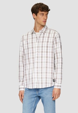 Chemise à carreaux blanche avec des lignes brunes, manches longues, poche poitrine unique et ourlet droit. Associée à un jean bleu clair.